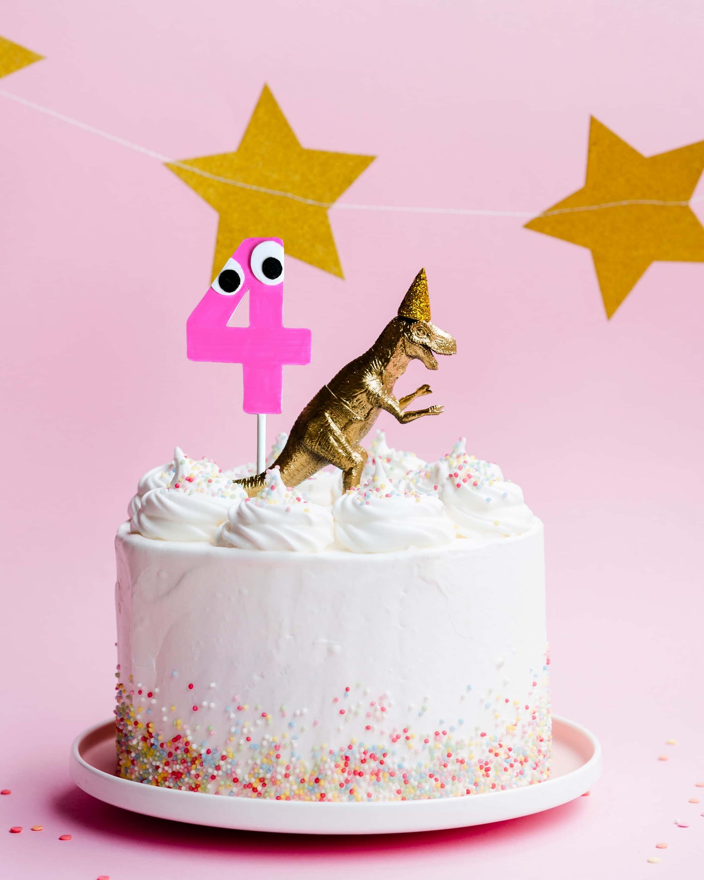Birthday cake with dinosaur topper and number 4 on a pink background