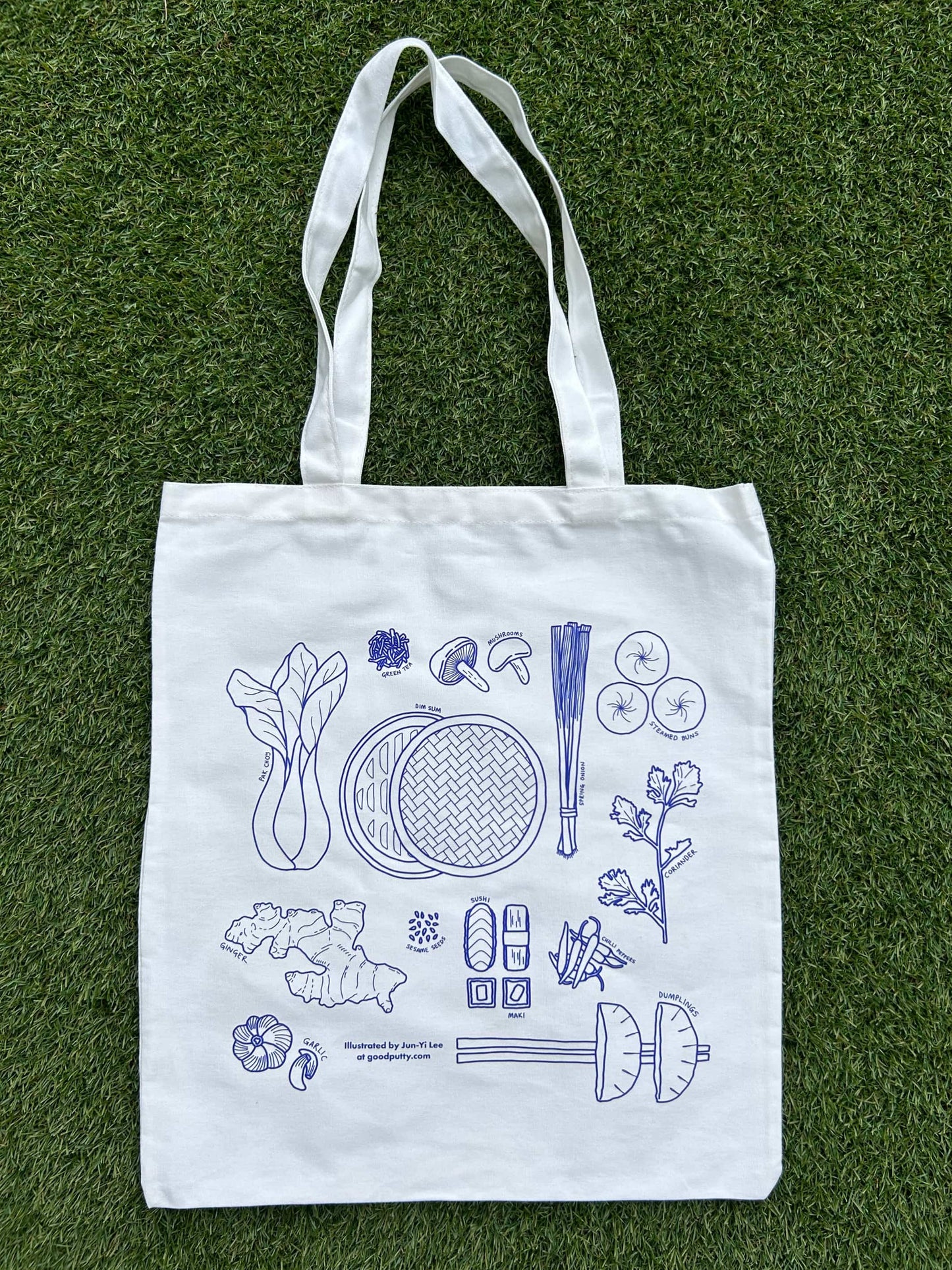 White tote bag with blue illustrations of Asian ingredients on a grass background