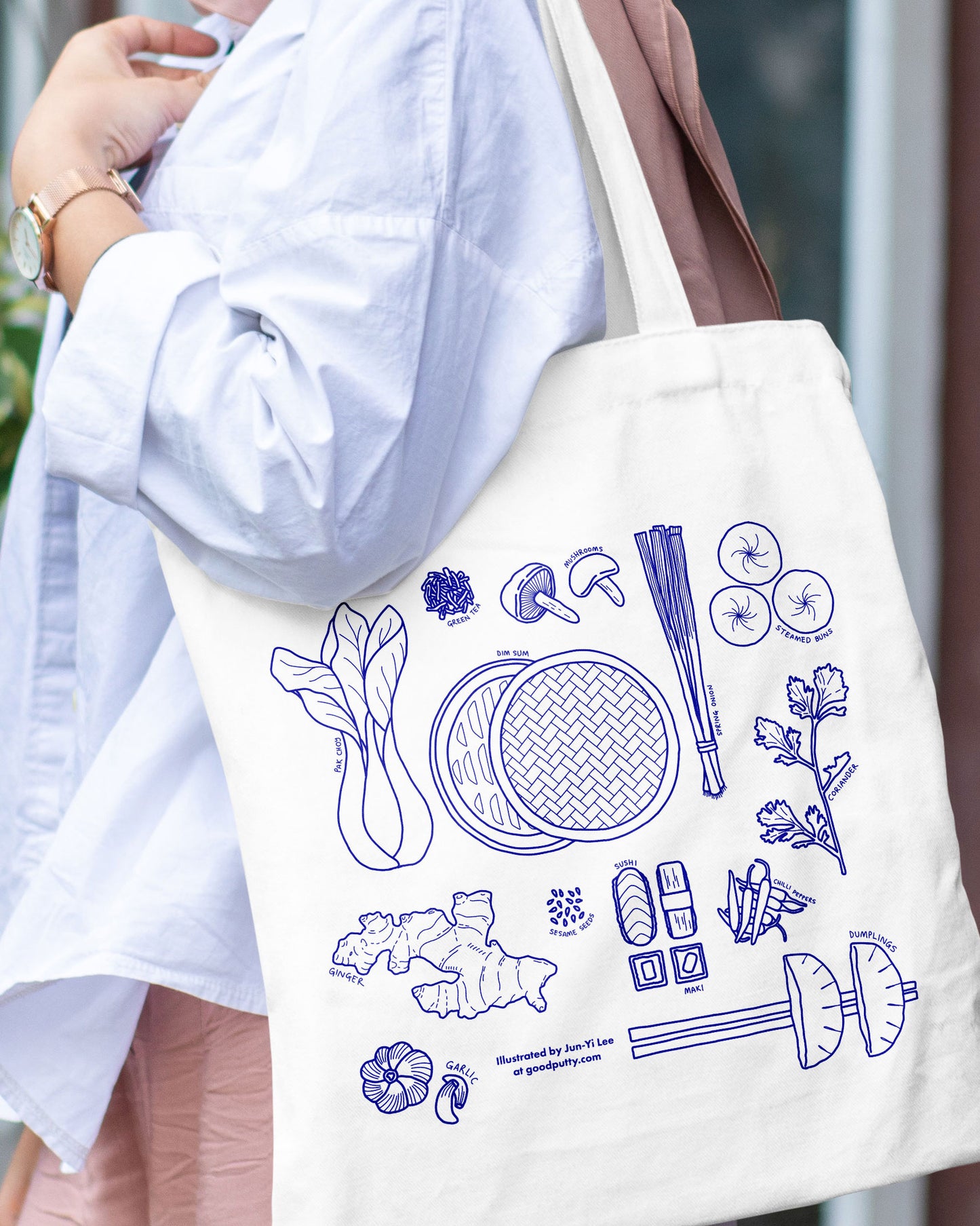 Person holding a tote bag with blue illustrations of Asian ingredients