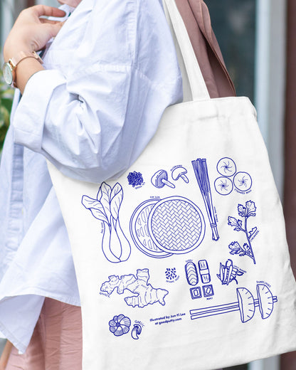 Person holding a tote bag with blue illustrations of Asian ingredients