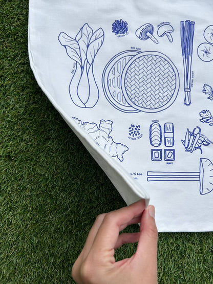 Closeup showing a white tote bag with blue illustrations of Asian ingredients