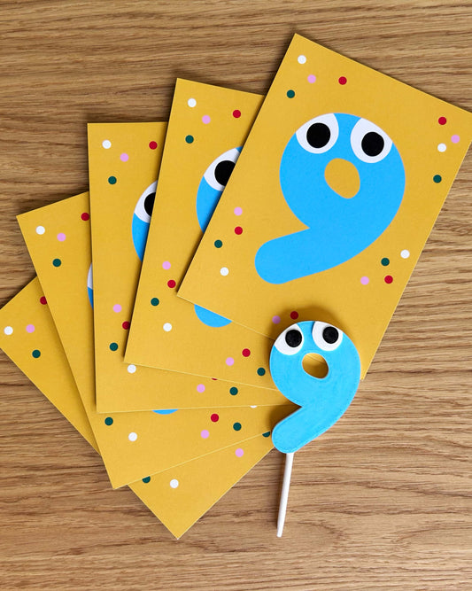 Yellow birthday invitations with blue number 9 designs and cake topper on a wooden surface