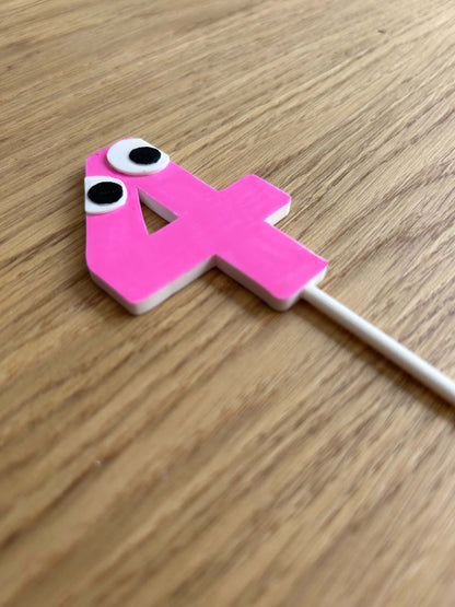 Pink number '4' cake topper with playful eyes on a wooden surface