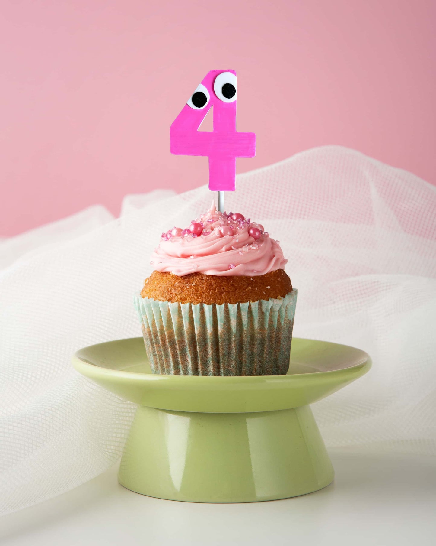 Cupcake with pink frosting and a number 4 candle on a green stand against a pink background