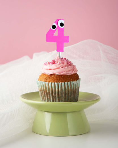 Cupcake with pink frosting and a number 4 candle on a green stand against a pink background