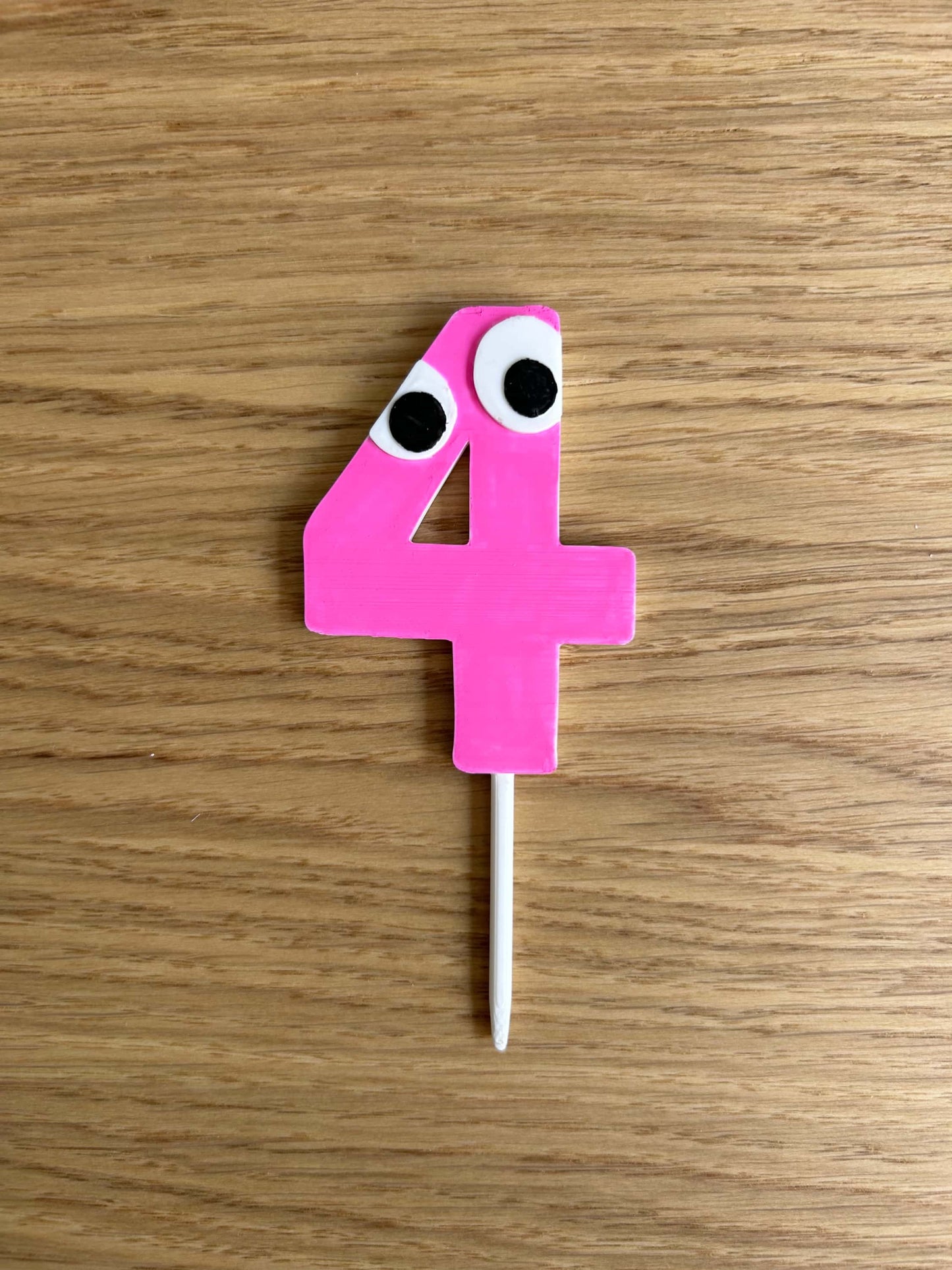 Pink cake topper in the shape of a "4" with googly eyes on a wooden surface