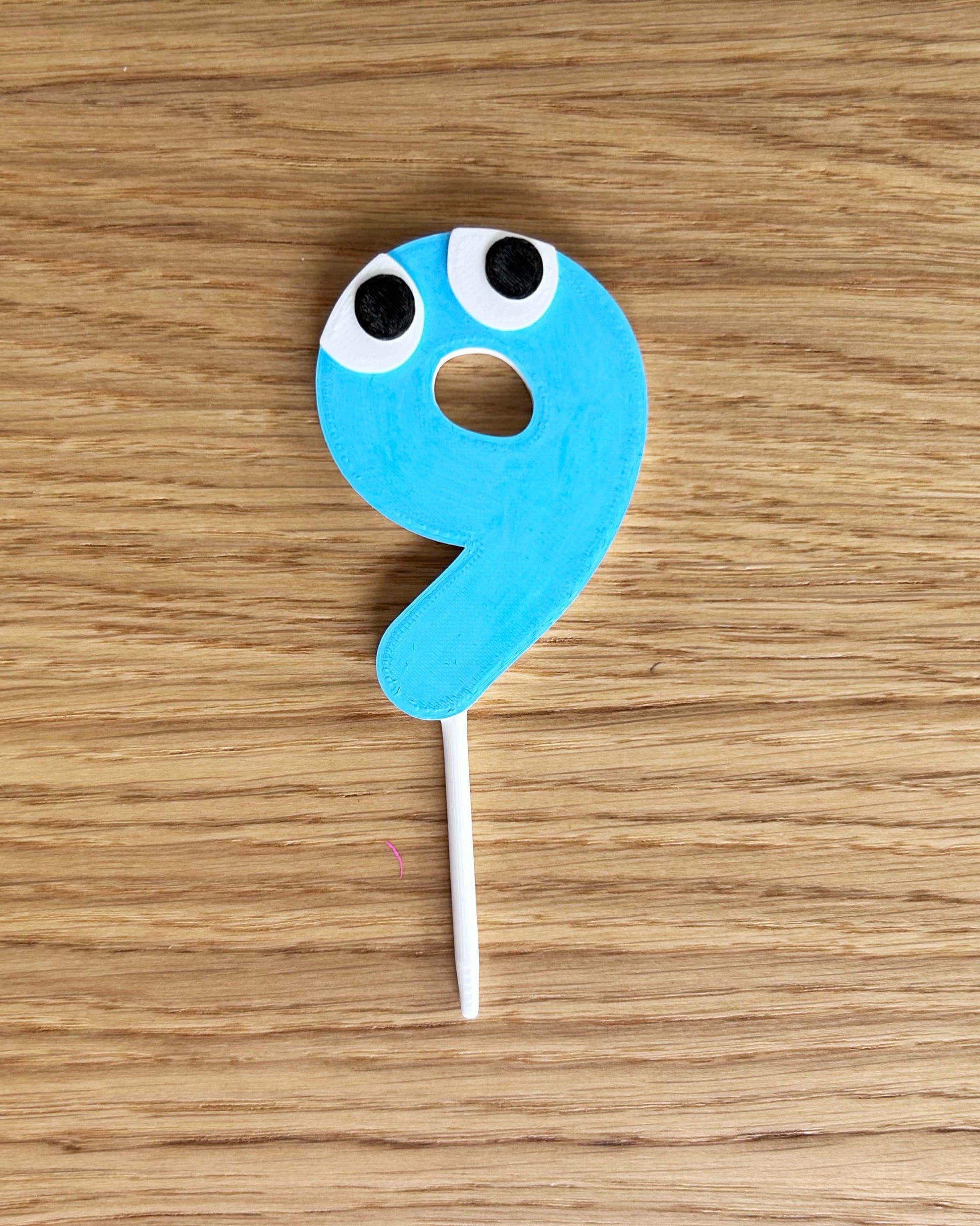 Blue number 9 cake topper with eyes on a wooden surface