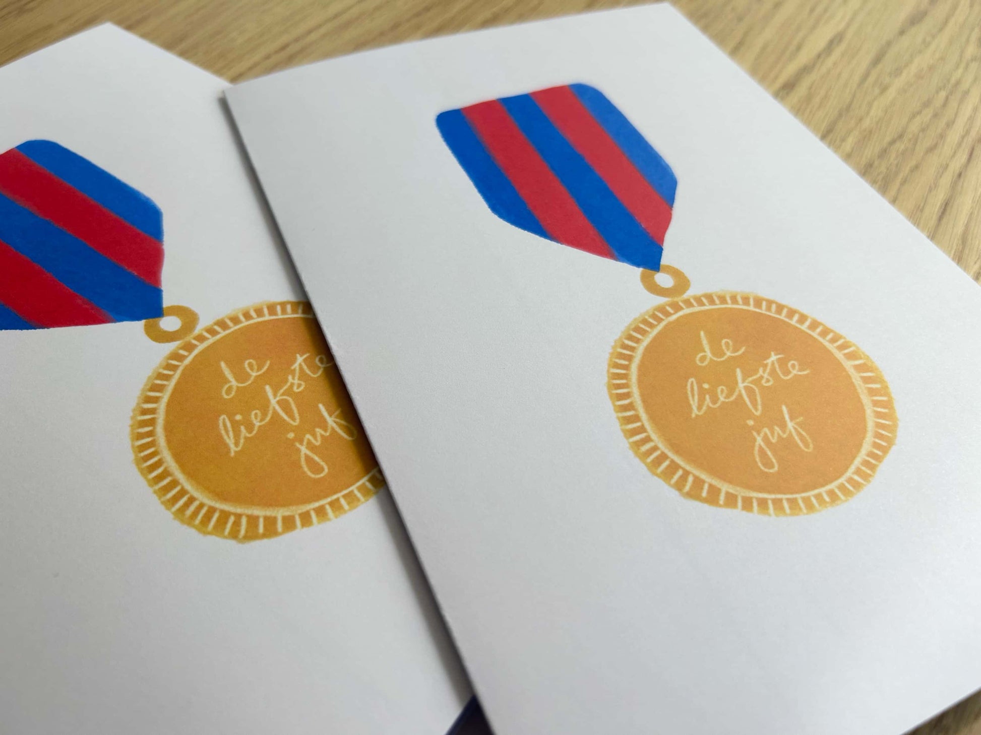 Two greeting cards with decorative ribbons and a gold medal design on a wooden surface.