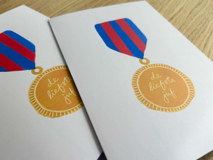 Two greeting cards with decorative ribbons and a gold medal design on a wooden surface.