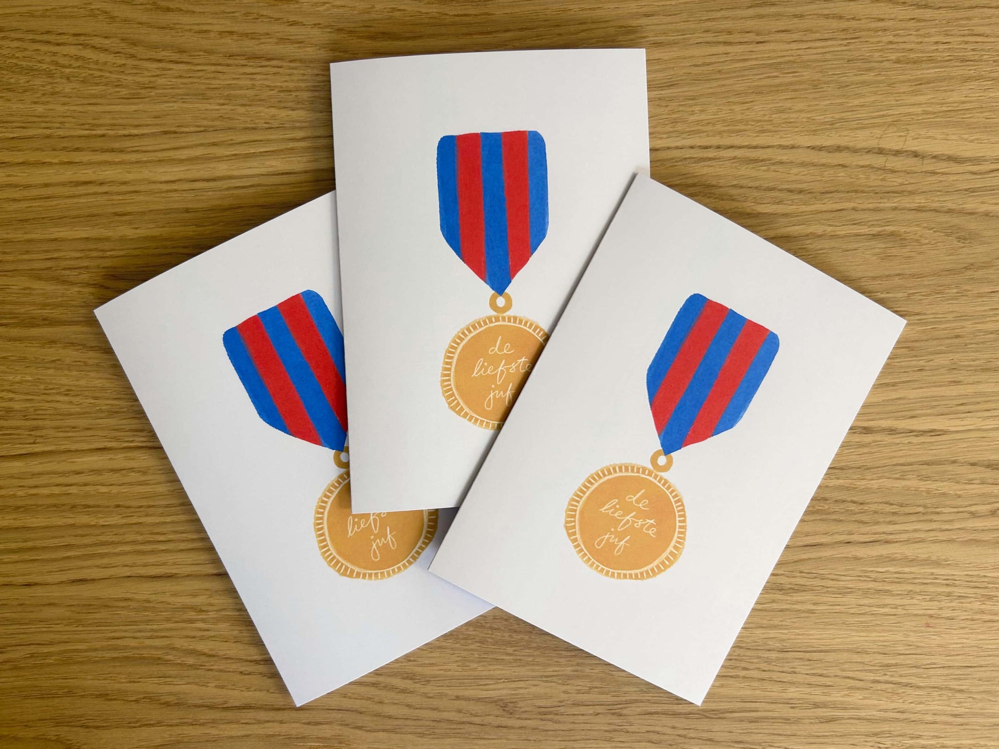 Three greeting cards with medal designs on a wooden surface