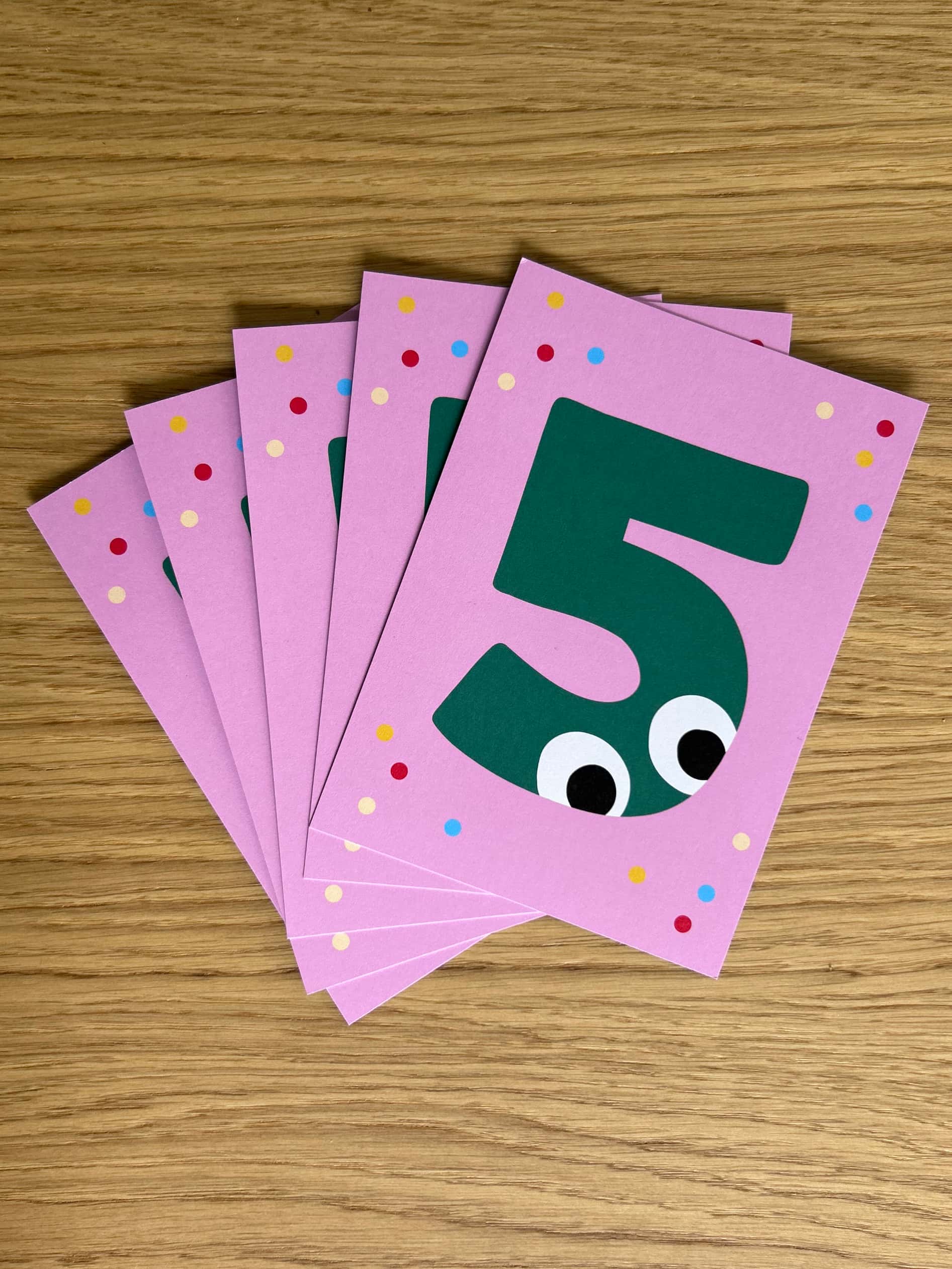 Stack of pink cards with green number 5 design on a wooden surface