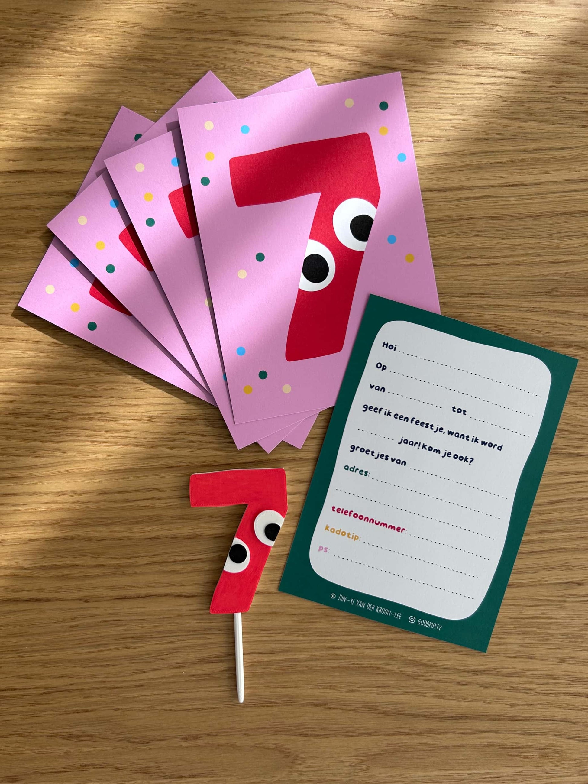 Red number 7 cake topper with googly eyes on a pink card, accompanied by a set of invitation cards
