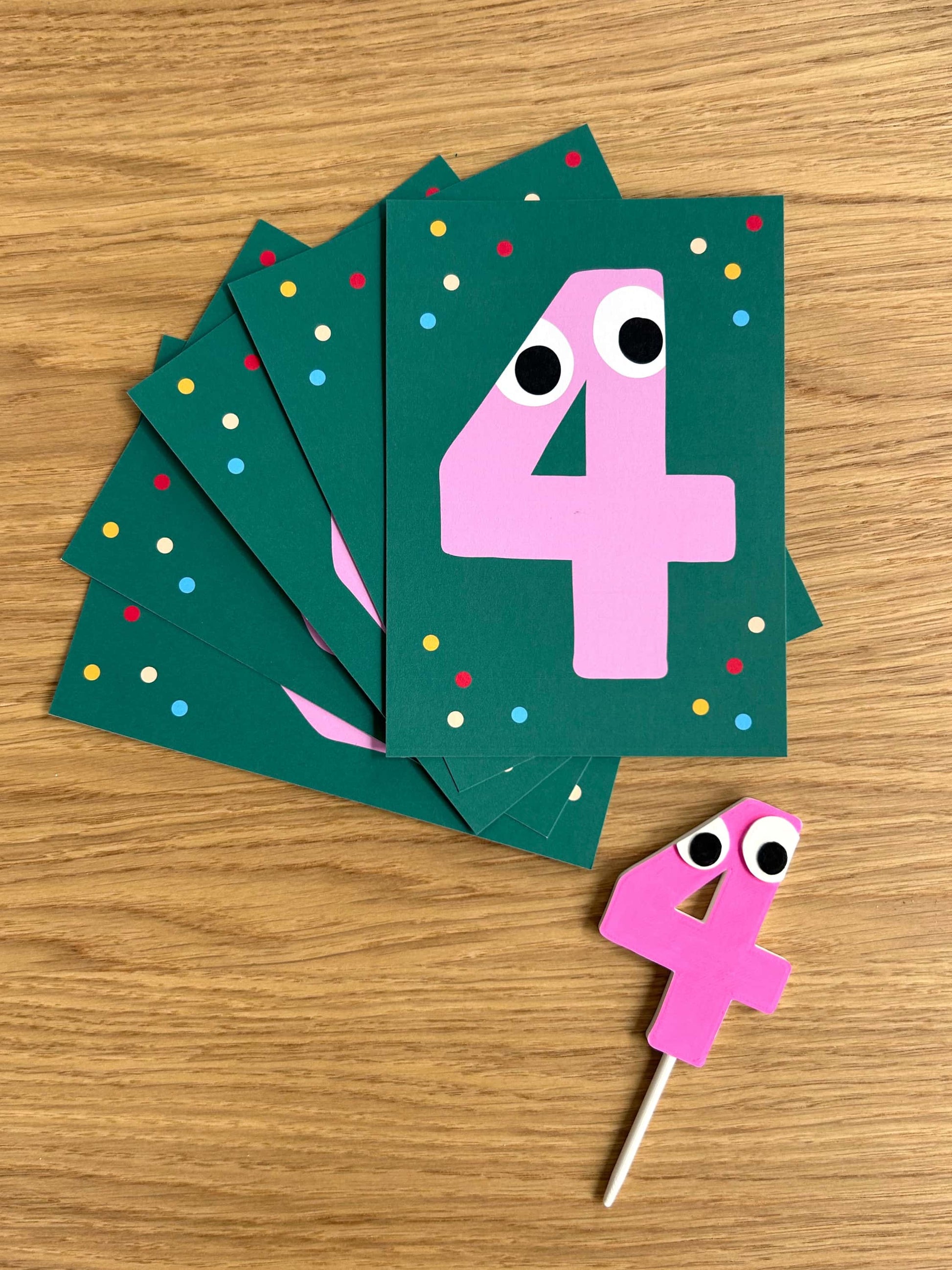 Birthday invitation cards with pink number 4 cake topper with googly eyes on a wooden surface
