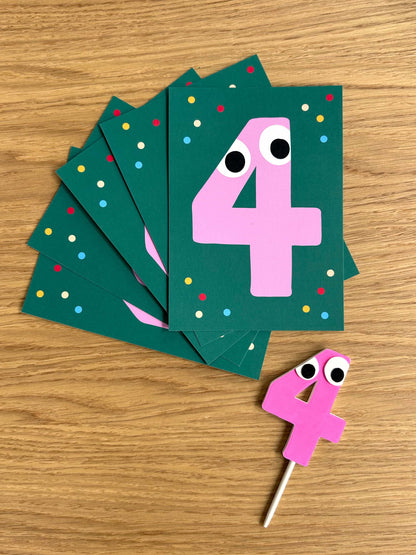 Birthday invitation cards with pink number 4 cake topper with googly eyes on a wooden surface
