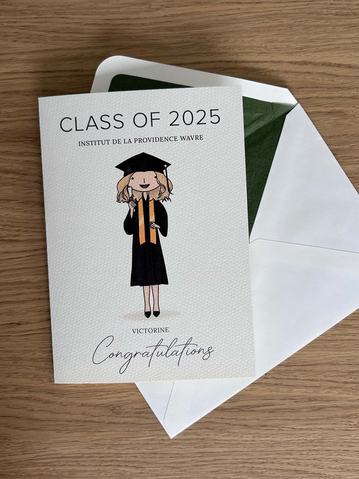 Graduation-themed card with a custom graduate illustration and 'Class of 2025' text, on a wooden surface.