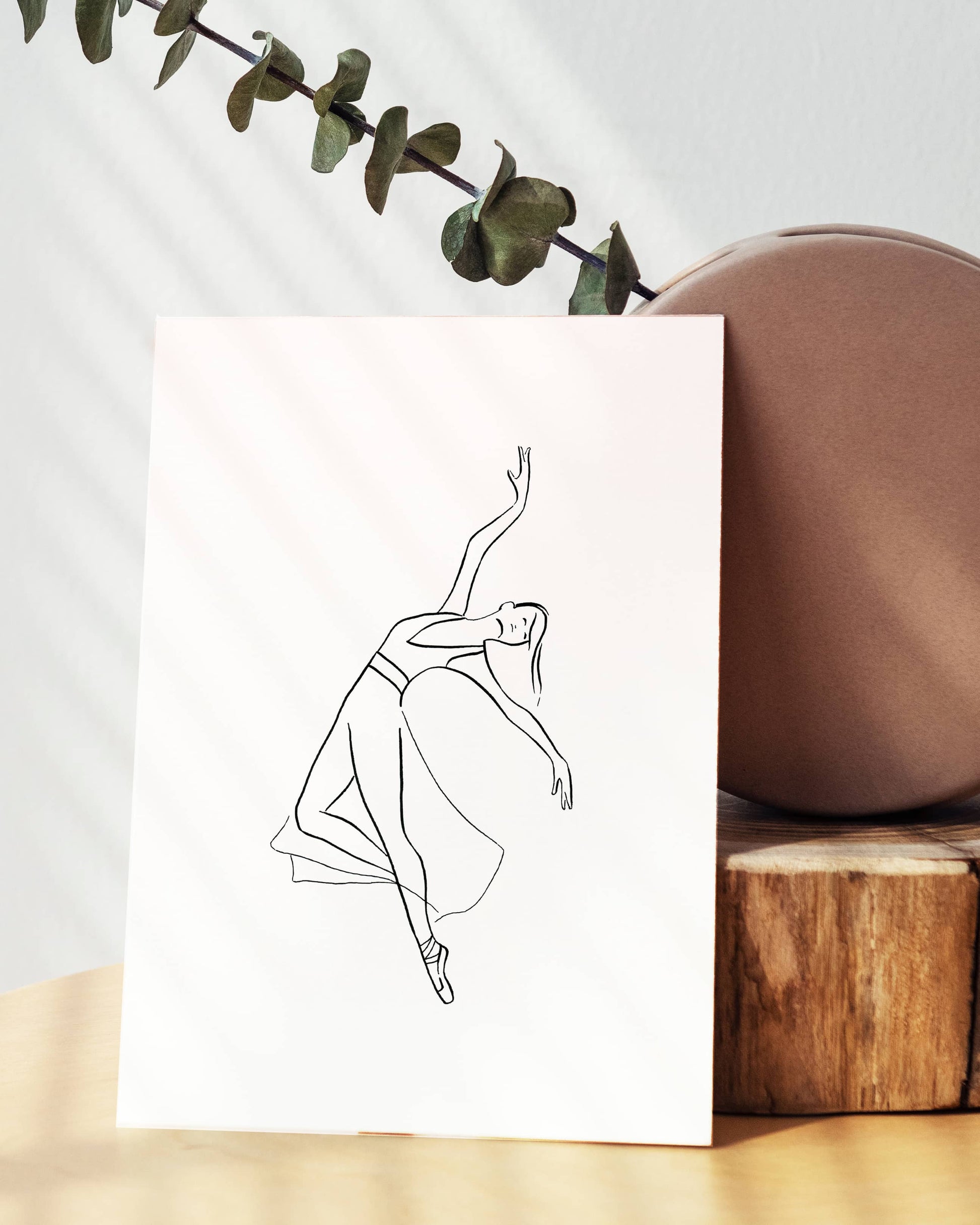 Line drawing of a dancer on a white card with a plant and wooden block in the background