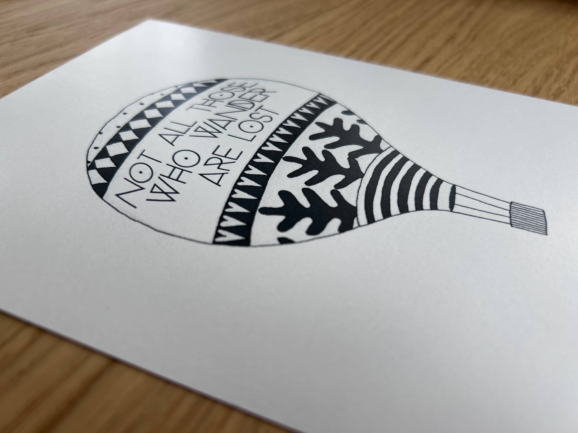 Black and white illustration of an air balloon with a traveller's quote by J.R.R. Tolkien on a white background