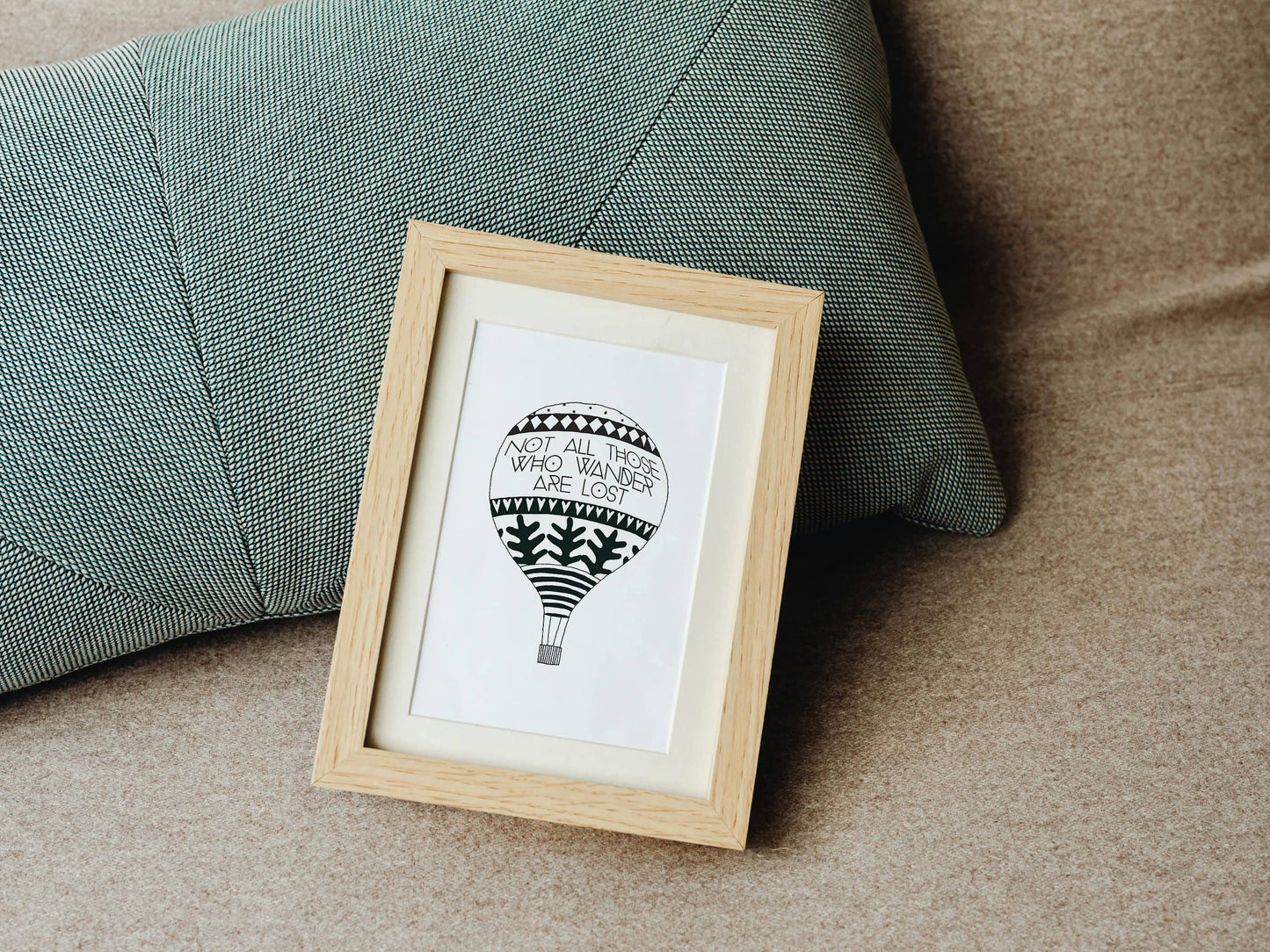 Framed artwork of a hot air balloon illustration with a traveller's quote by J.R.R. Tolkien on a couch