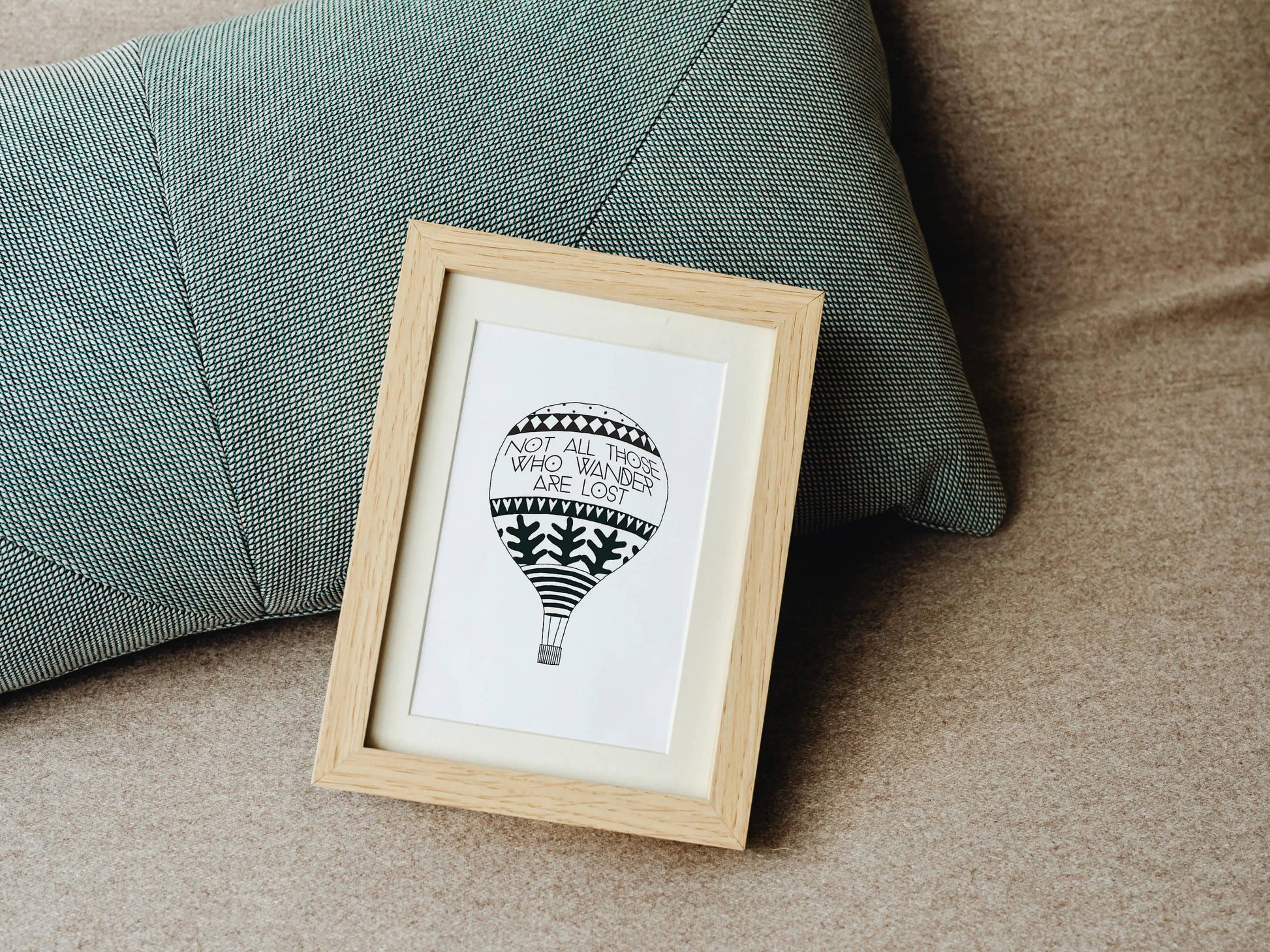 Framed artwork of a hot air balloon illustration with a traveller's quote by J.R.R. Tolkien on a couch