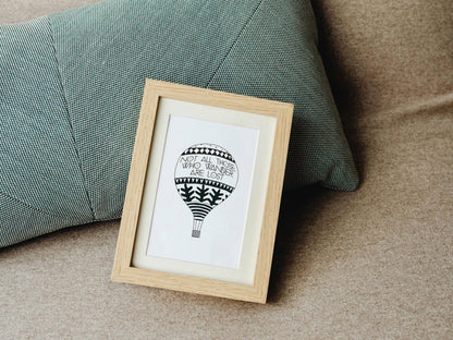 Framed artwork of a hot air balloon illustration with a traveller's quote by J.R.R. Tolkien on a couch