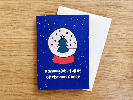 Greeting card with snow globe design and Christmas tree on a wooden surface