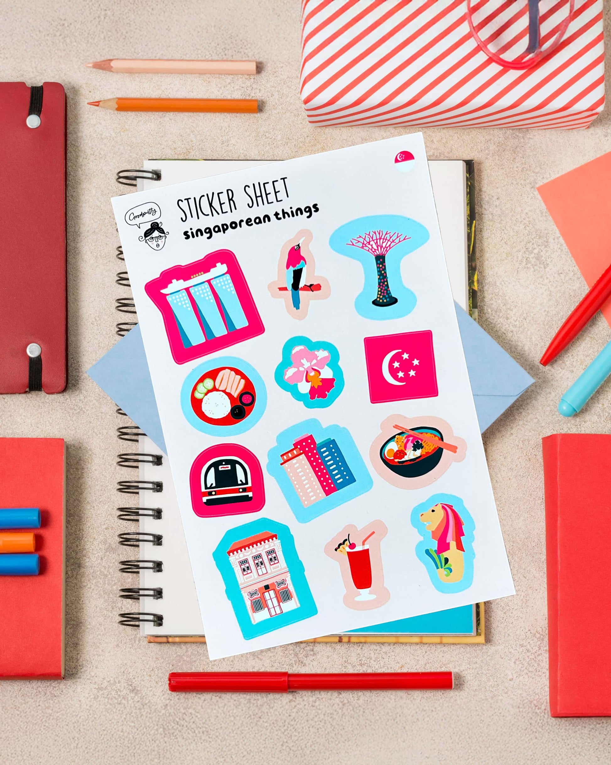 Sticker sheet with colorful Singapore-themed illustrations on a notebook surrounded by stationery items.